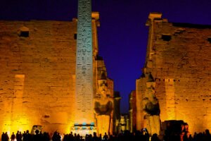 Illuminated statues and columns of Luxor Temple glowing at night under a dark sky.